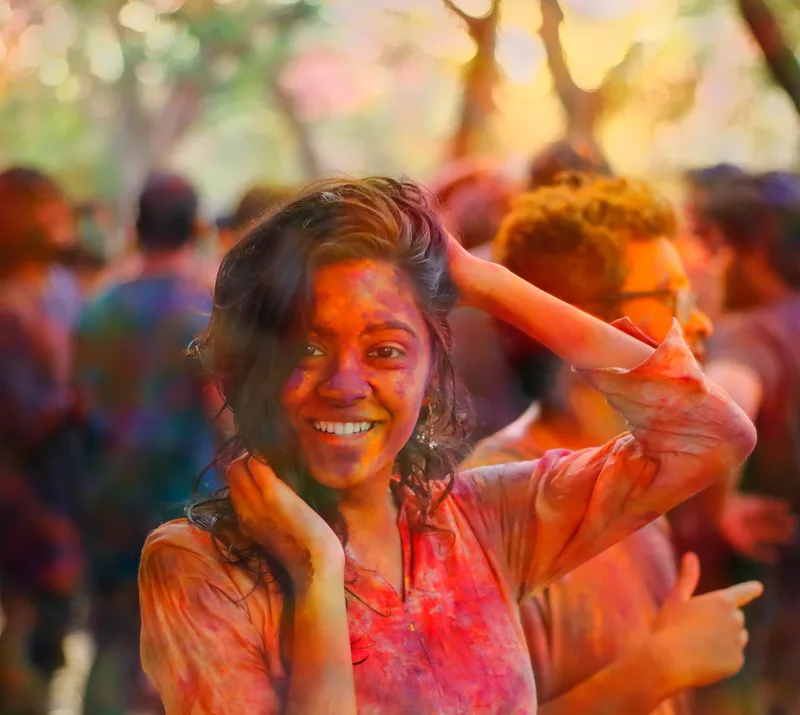 A young woman laughing at Holi, her face covered in colour.