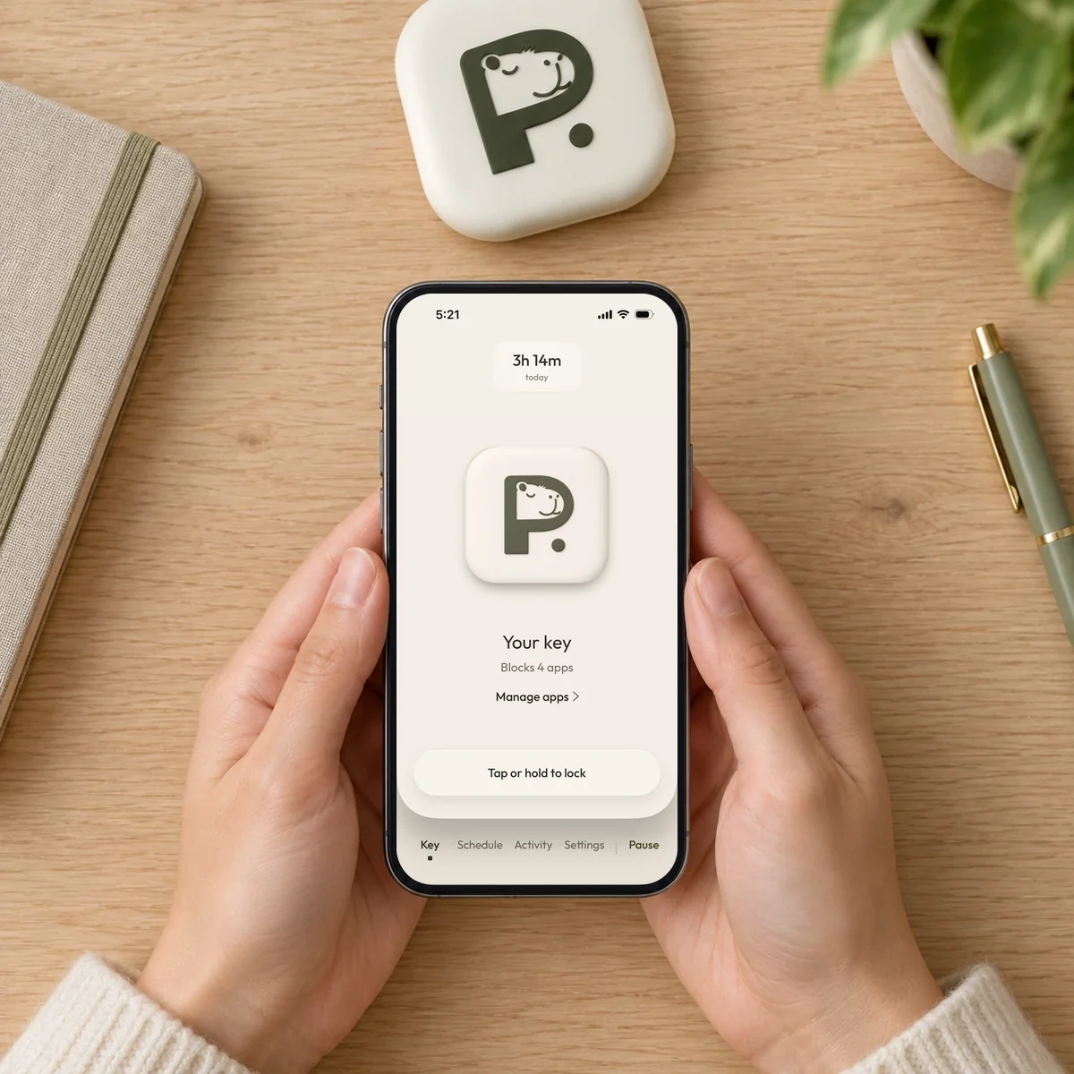 Hands holding a phone showing the Pause app Key screen, with the Pause Device on the desk above it.